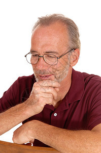 一个老人坐在椅子上手放下巴想着用玻璃杯为白色背景而孤立图片