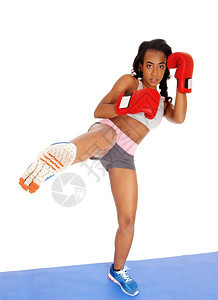一个瘦弱的非裔美国女孩站在蓝色垫子上参加拳击练习时一只腿抬起来戴着红色手套图片