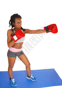 一个瘦弱的非裔美国女孩在拳击练习时站在蓝垫子上戴着红色手套被白背景隔离图片