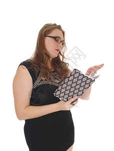 一个金发美女穿着黑色礼服和眼镜站在腰上读她的日记与白种背景隔绝图片