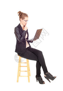 一位年轻的金发女商人坐在椅子上工作她的笔记本电脑上黑色的紧身衣和外套上图片