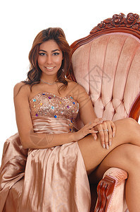 身着金色晚礼服的可爱年轻女子坐在椅上双腿侧面与白色背景隔绝图片