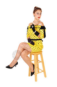 一位穿着黄色裙子的年轻美女拿着长烟筒坐在椅子上与白种背景隔绝图片