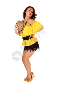 一个可爱的年轻女子穿着黑色短裤和黄上衣戴着牛仔帽与白背景隔绝图片