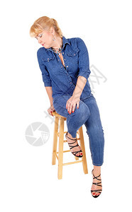 一个穿着牛仔裤和夹克的金发美女坐在酒吧的椅子上看着现场被白种背景隔离图片