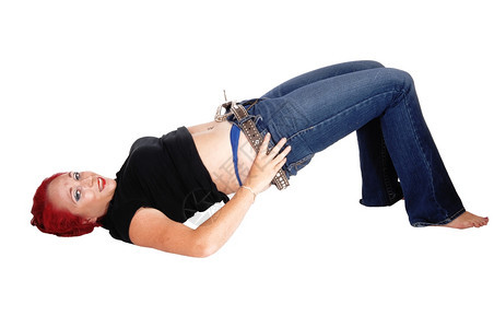 一个躺在地上的女人试图拉起她的牛仔裤红色头发孤立的白色背景图片
