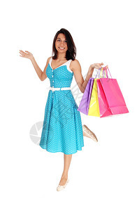 一个穿着蓝裙子的快乐年轻女人拿着一些彩色购物袋微笑着与白种背景隔绝图片