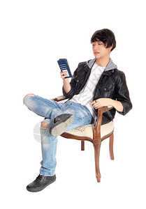 一个穿着黑皮夹克的英俊亚洲男子坐在一把旧扶手椅上坐在他的手机上说话图片