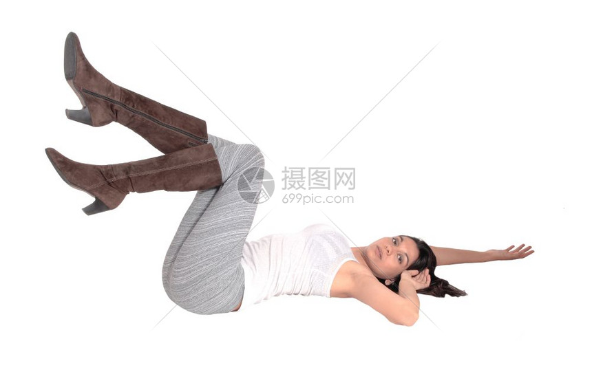 一个可爱的西班牙年轻女人躺在灰色的腿上一双靴子在地板上与白种背景