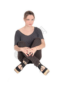 穿着牛仔裤和黑发的美丽年轻女子坐在地上双腿穿看起来很严重与白种背景隔绝图片