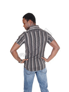 身穿条纹衬衫和牛仔裤的非裔美国人男子背靠向下仰望手伸臀部因白背景被孤立图片