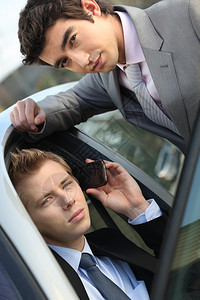 两名青年商人坐在汽车里用手机说话图片