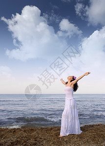 穿白衣服的女人在海边张开双手云空背景图片