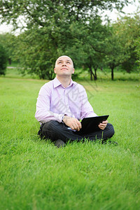 手持笔记本电脑的商人在公园绿草地上图片