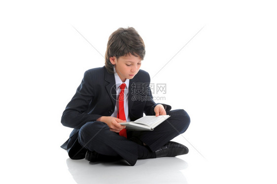 穿着商业西装的小男孩在看坐地板上的一本书图片