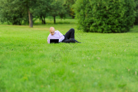 手持笔记本电脑的商人躺在公园绿草上图片