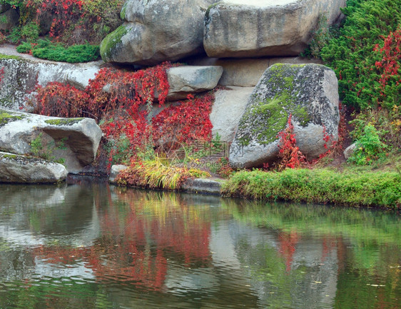 秋季公园中大石头反射而成的池塘水面图片