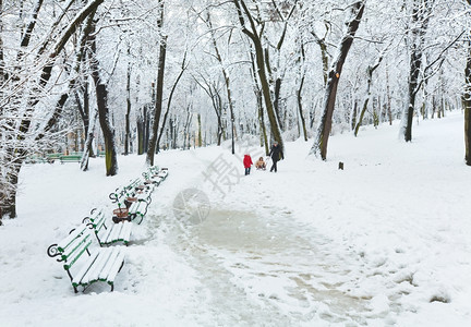 母亲与子女在冬季雪中行走的婴儿在城市公园日落图片