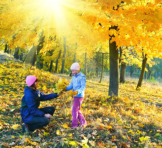 幸福的家庭母亲与女儿在金色的阳光秋天公园中行走图片
