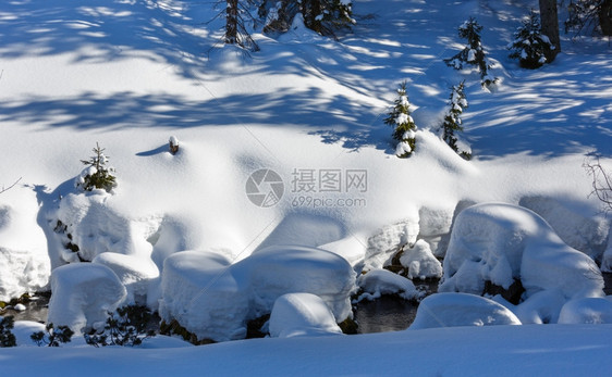 冬雪山丘上长着小毛树溪流在雪地下图片