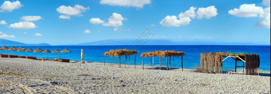 夏晨沙滩,有防晒床、树冠和白石块(阿尔巴尼亚,伯什)蓝天有云层三缝全景。图片