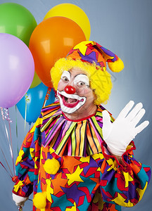 友好的马戏团小丑拿着一堆气球挥手打招呼图片