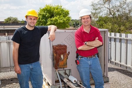两名空调修理技术人员站在一个工业压缩机房前的屋顶上图片