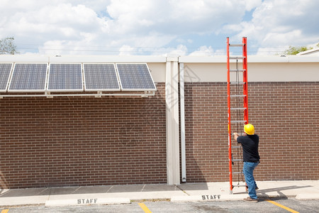 建筑工人准备爬上楼顶在太阳能电池板上工作的大视角图片