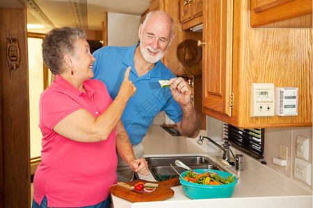 退休的老年夫妇在家中的汽车厨房做午餐丈夫等不及吃午饭了图片