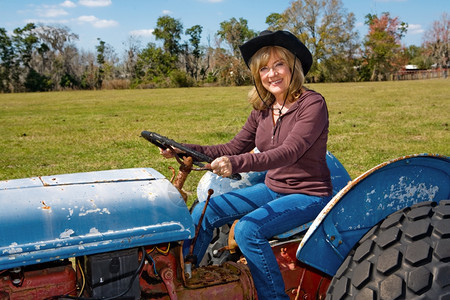 美丽的成熟女人驾驶拖拉机在她的农场图片