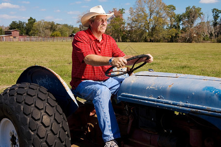 英俊成熟的牛仔骑着拖拉机穿过田地图片