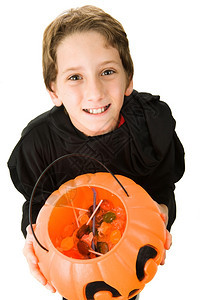 可爱的小男孩穿着神圣的服装拿着一个满糖果的南瓜桶图片