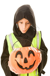 可爱的小男孩穿着他神圣服装和反射式安全背心在南瓜桶里吃着糖果图片
