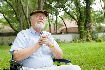 坐在轮椅上祈祷的老人在一个美丽的户外场所图片