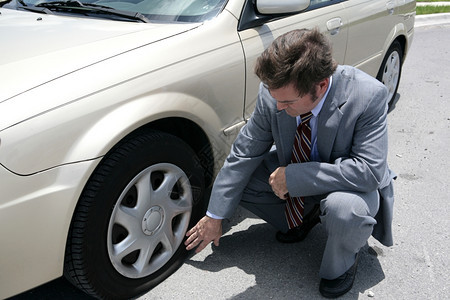 一个穿着衣服参加商业会议的人在他车里发现了一个轮胎爆图片
