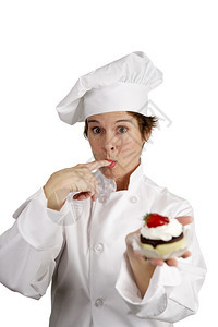 一个漂亮的厨师拿着草莓芝士蛋糕饼舔她手指上的奶油图片