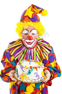有趣的小丑在生日蛋糕上吹蜡烛白纸孤立图片