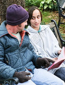 无家可归的父亲和儿子读圣经或一个为穷人服务的十几岁志愿者背景图片