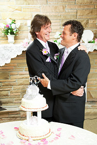 两个穿着礼服的帅哥男同志在婚礼招待会上拥抱爱婚礼蛋糕和玫瑰花瓣图片