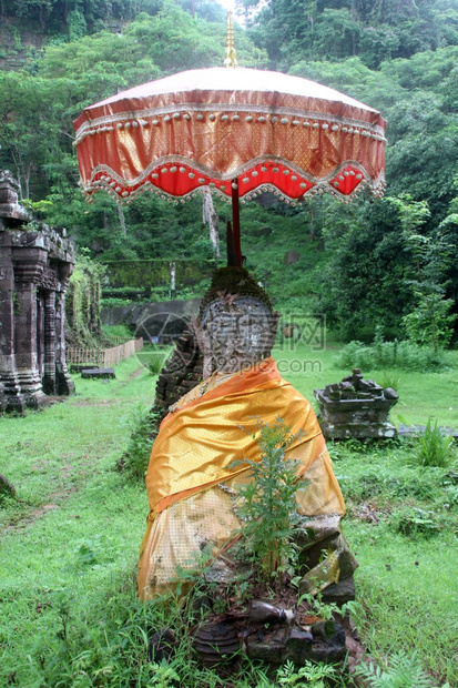 老挝WatPhu的旧佛像在雨伞下图片