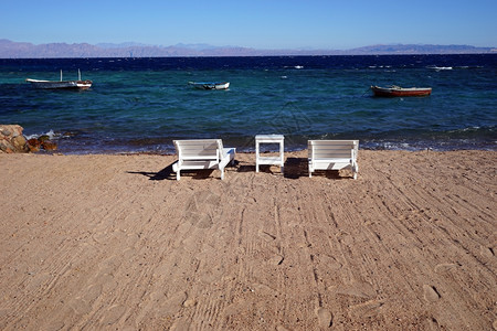 埃及达哈布船只附近的沙滩上白木床和桌子图片