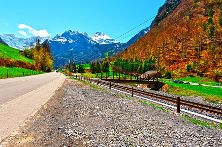 与瑞士雪峰阿尔卑斯山背景的铁路平行高速公图片