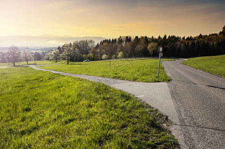 日出时瑞士牧场之间的风沥青路有草地的瑞士风景和有交通标志的十字路口图片