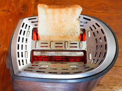 在木制桌上热金属烤面包机上一片图片