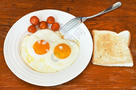 白盘上的两个炸鸡蛋樱桃和桌上的吐司图片
