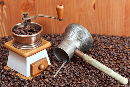 木墙附近许多烤咖啡豆上的旧式手制咖啡研磨机和铜锅图片