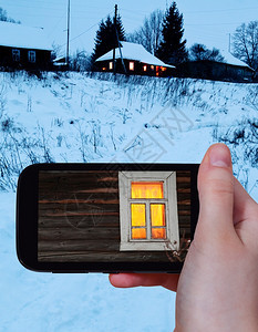 旅行概念旅游者用智能手机拍摄冬季农村原木屋黄光灯窗的照片图片