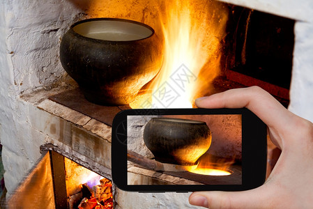 摄影食品概念旅游者拍摄俄罗斯炉灶和旧铸铁锅的火道以及智能手机上的炉叉图片