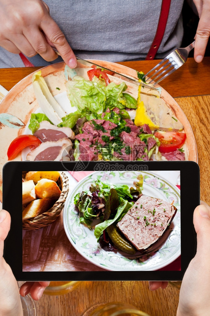 拍摄食物的概念游客拍摄法国肉食在餐厅的盘子上智能手机图片