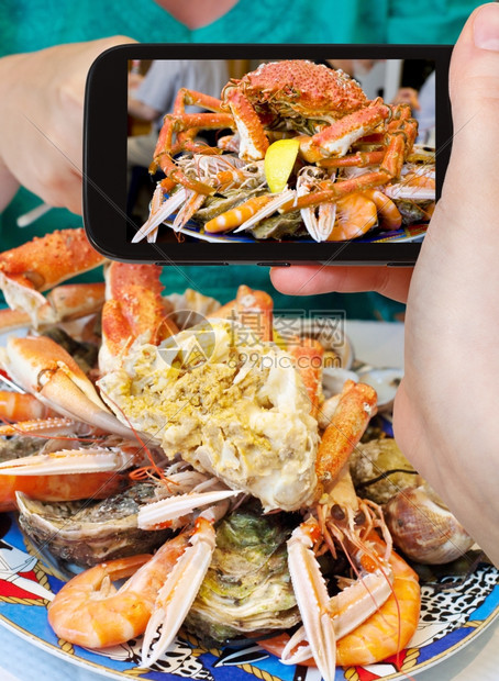拍照食品概念旅游者用蟹虾和智能手机拍摄海鲜盘法国图片